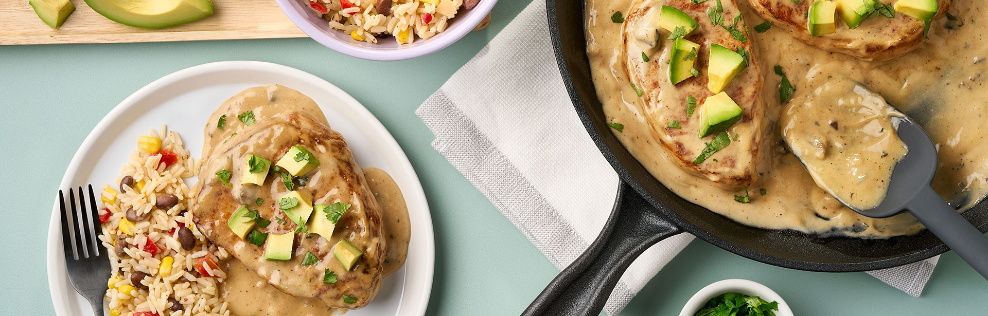 An image of prepared Avocado Ranch Pork Chops and Rice showing seasoned Southwest vegetable blend, ranch dressing mix, long grain white rice, pork chops, Campbell's® Condensed Cream of Mushroom Soup, cilantro and avocado.