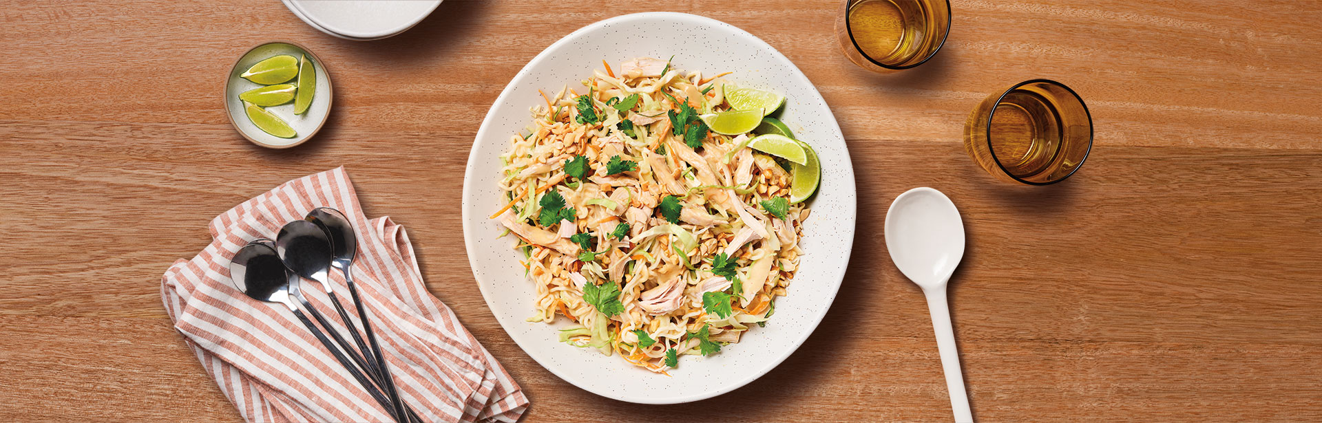An image of prepared Spicy Peanut Chicken Ramen showing ramen noodles with creamy peanut butter, Campbell's® Condensed Cream of Chicken soup, Swanson® Unsalted Chicken Broth, soy sauce, sriracha, cooked chicken or turkey and coleslaw mix topped with fresh cilantro and lime.
